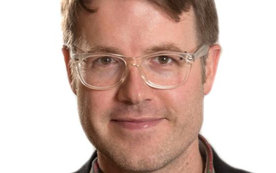 Image of Professor Matthew Chrisman. He has short brown hair and clear framed glasses and wears an open neck shirt with a t-shirt underneath and a jacket