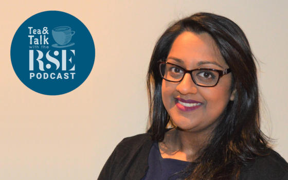 Talat Yaqoob is female with long black hair with brown tortoiseshell glasses, standing in front of a cream wall.