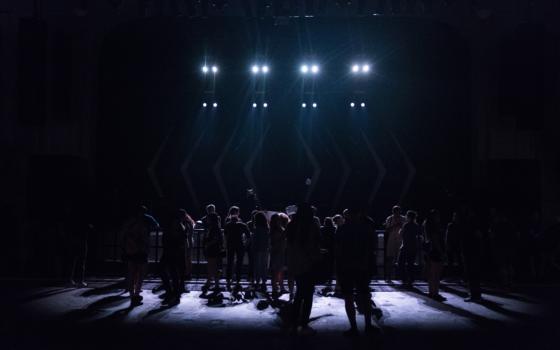 People are silhouetted in front of a stage lit by blue spotlights.