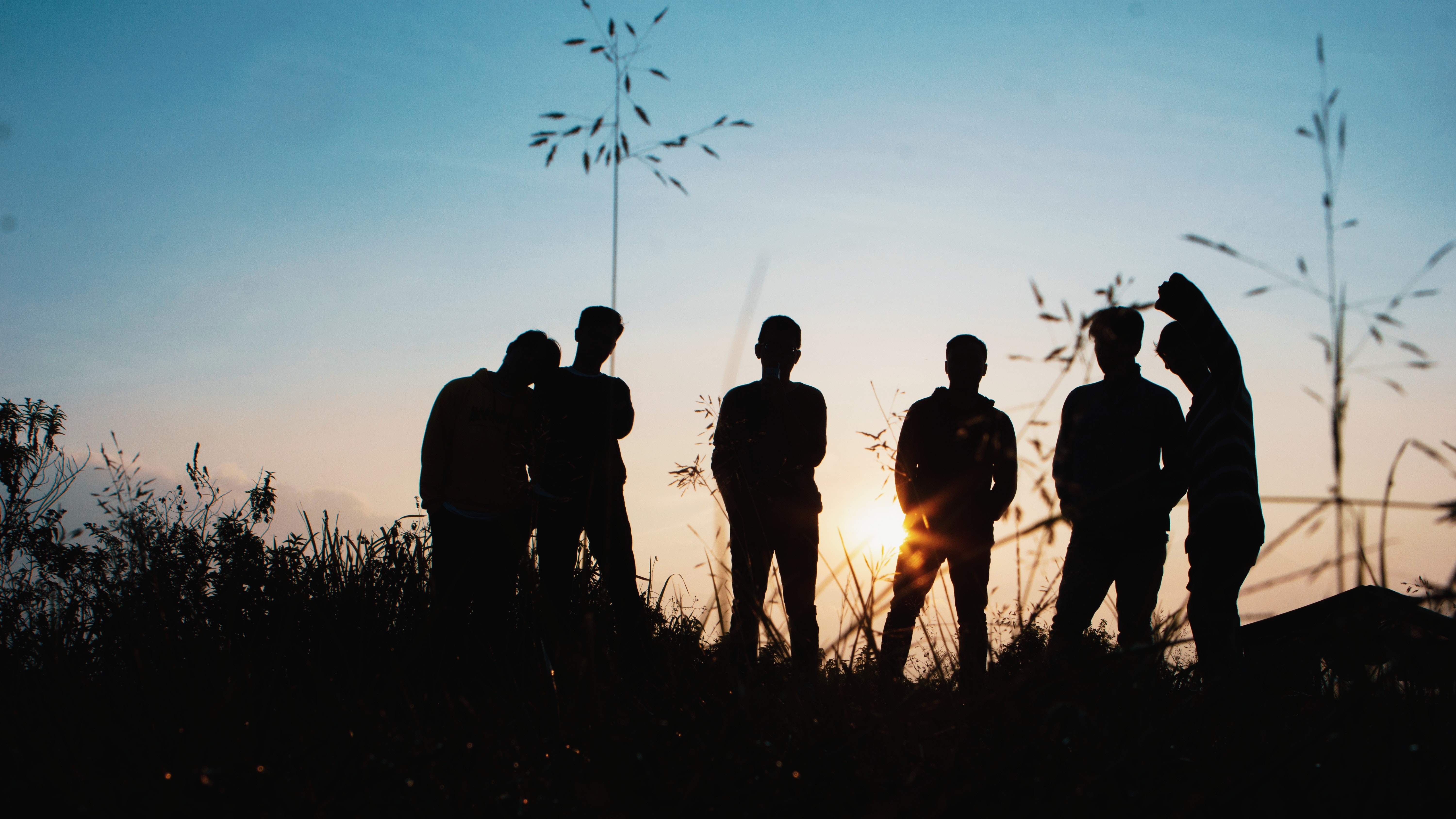 A group of teenagers stand silhouetted against a blue sky.