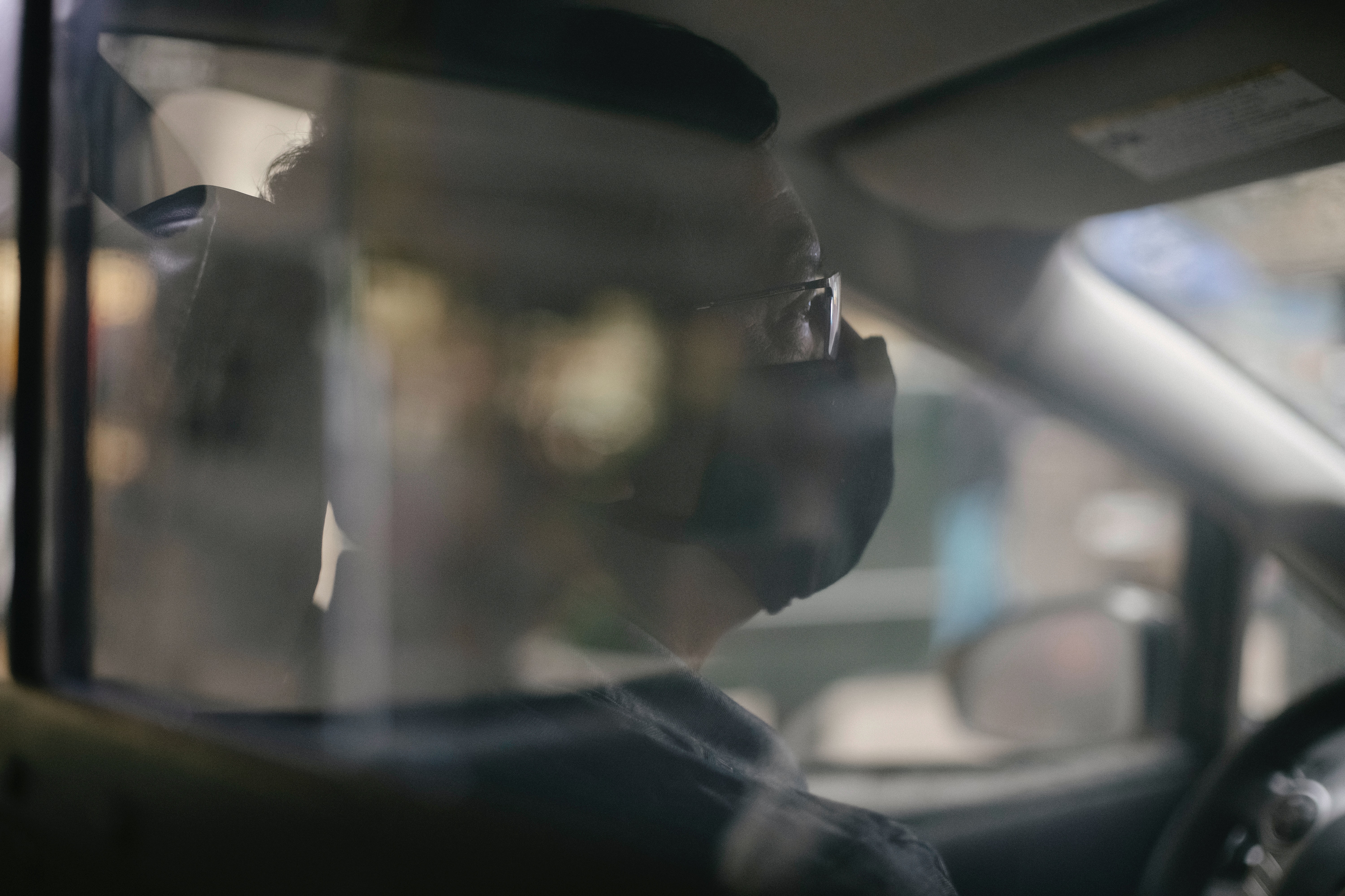 A man wearing a face mask is visible driving through the screen of a taxi cab.