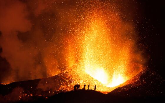 Figures are silhouetted in front of a volcanic eruption.