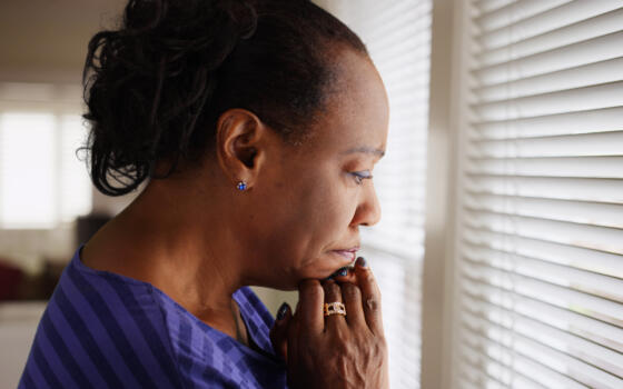 A black adult woman looks sadly out of a window.