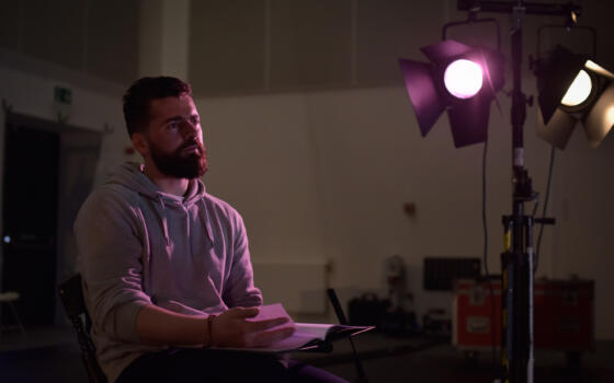 A side-lit seated man reads form a script.