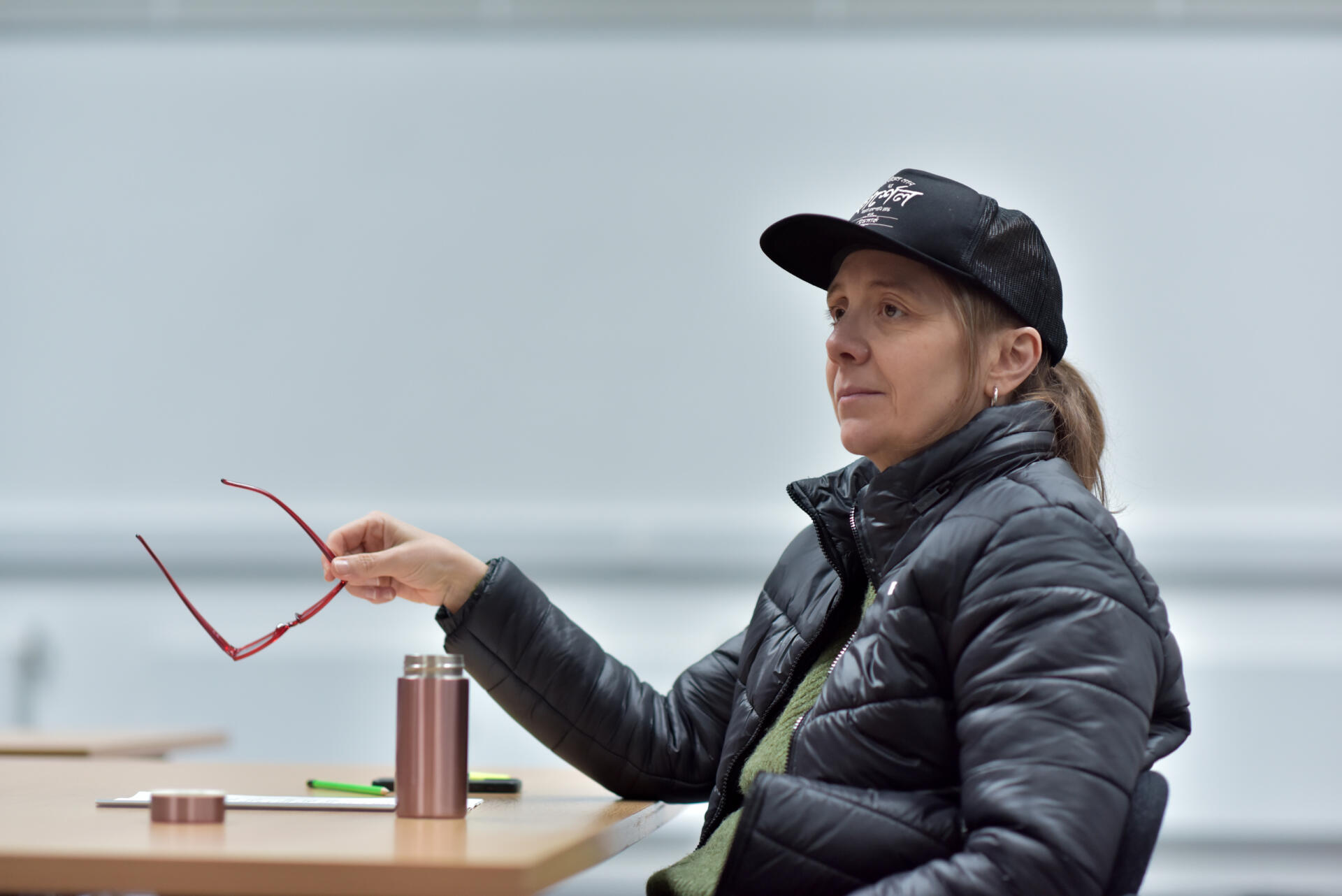 A woman sits, holding a pair of glasses, in rehearsal.